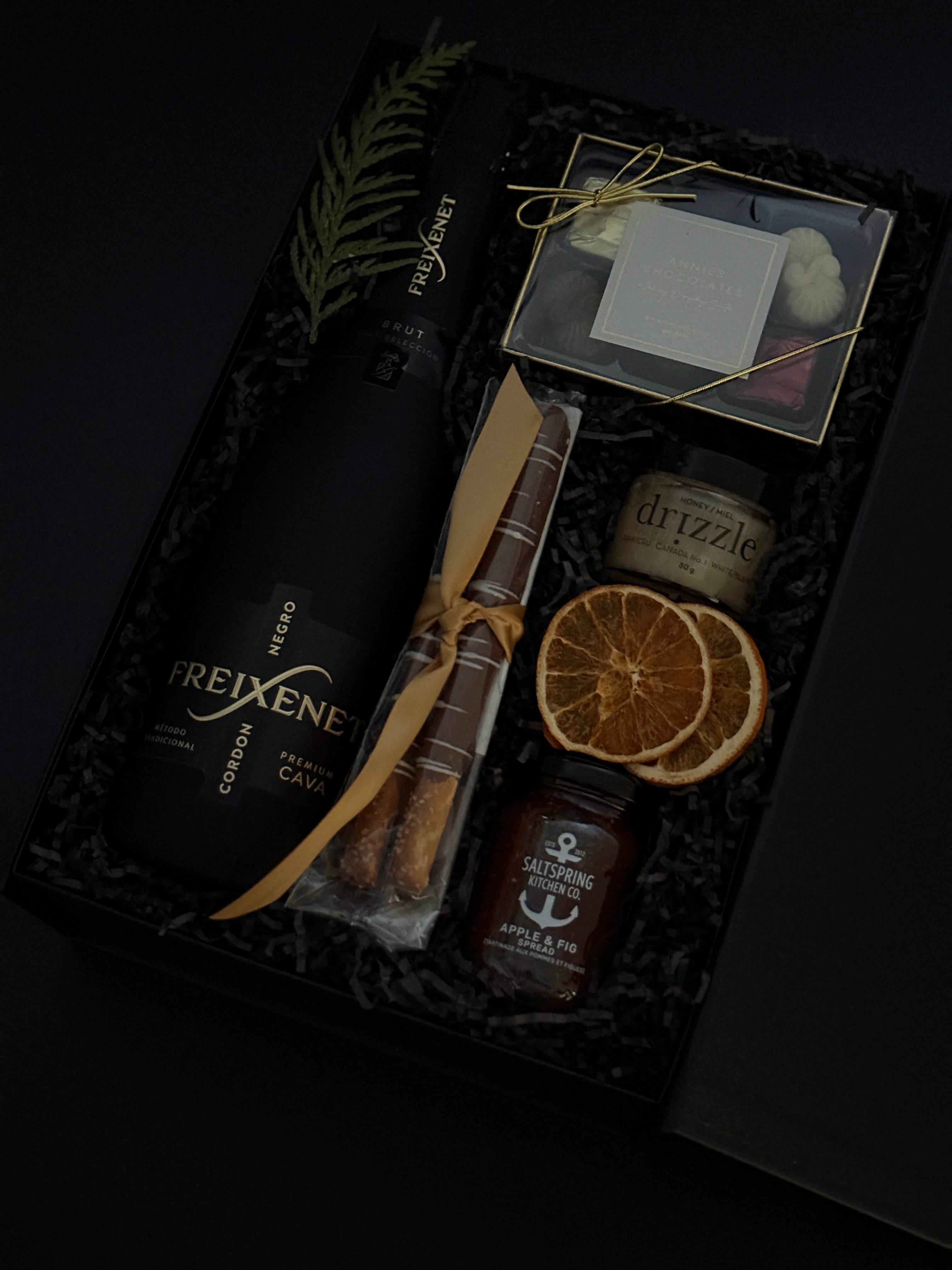 Obsidian Celebration Box with sparkling wine, chocolates, pretzels, honey, and fig spread arranged in a black gift box with festive greenery and ribbon.