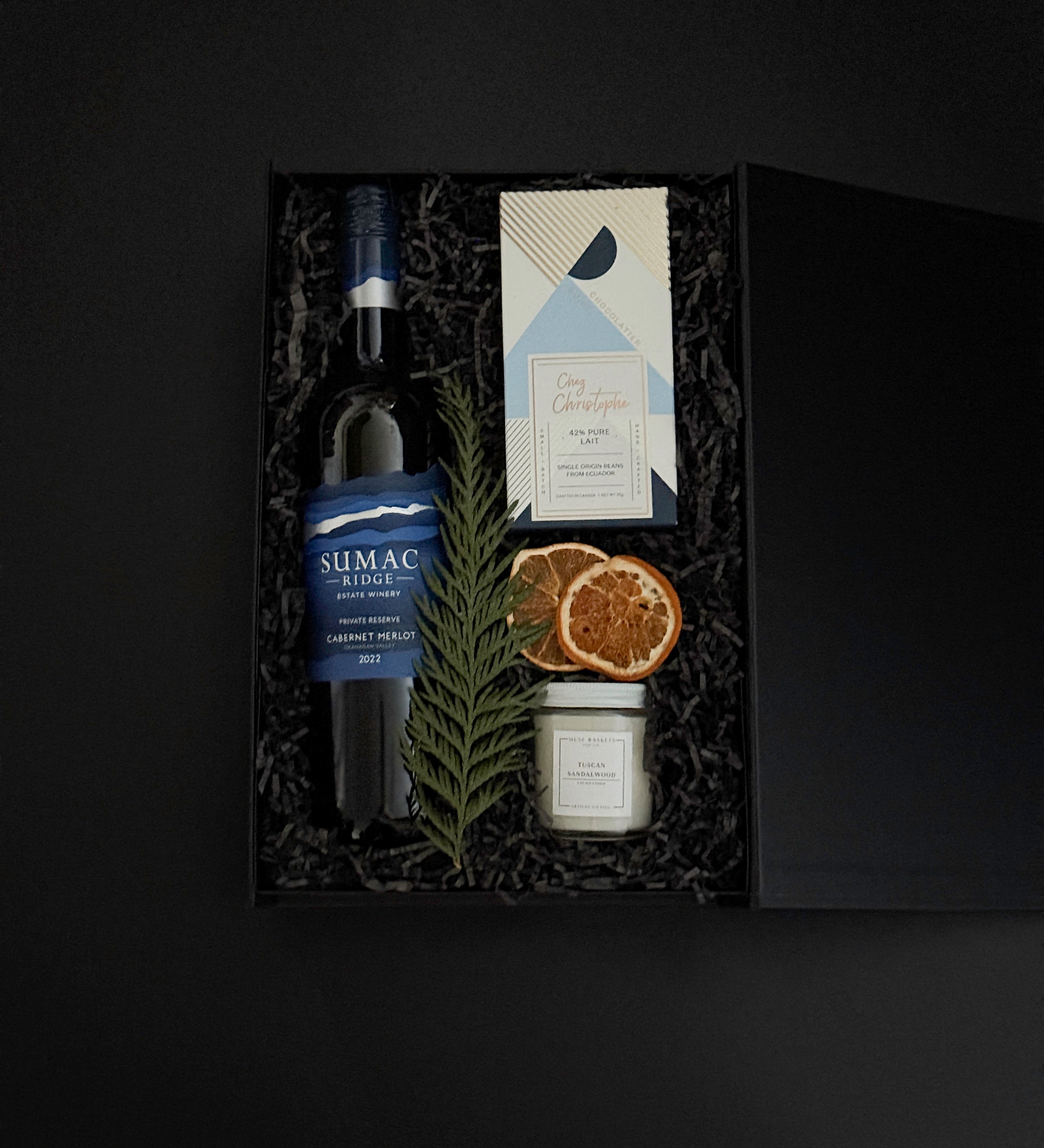 luxury black gift box with Cabernet Sauvignon, artisan chocolate, gold tin candle, and festive greenery, tied with grosgrain ribbon for a refined presentation.