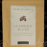 A stand-up pouch of Muse Baskets 'Classique au Lait' artisan hot chocolate, featuring a beige kraft paper exterior and a white label with brown cocoa bean graphics.