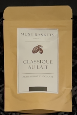 A stand-up pouch of Muse Baskets 'Classique au Lait' artisan hot chocolate, featuring a beige kraft paper exterior and a white label with brown cocoa bean graphics.