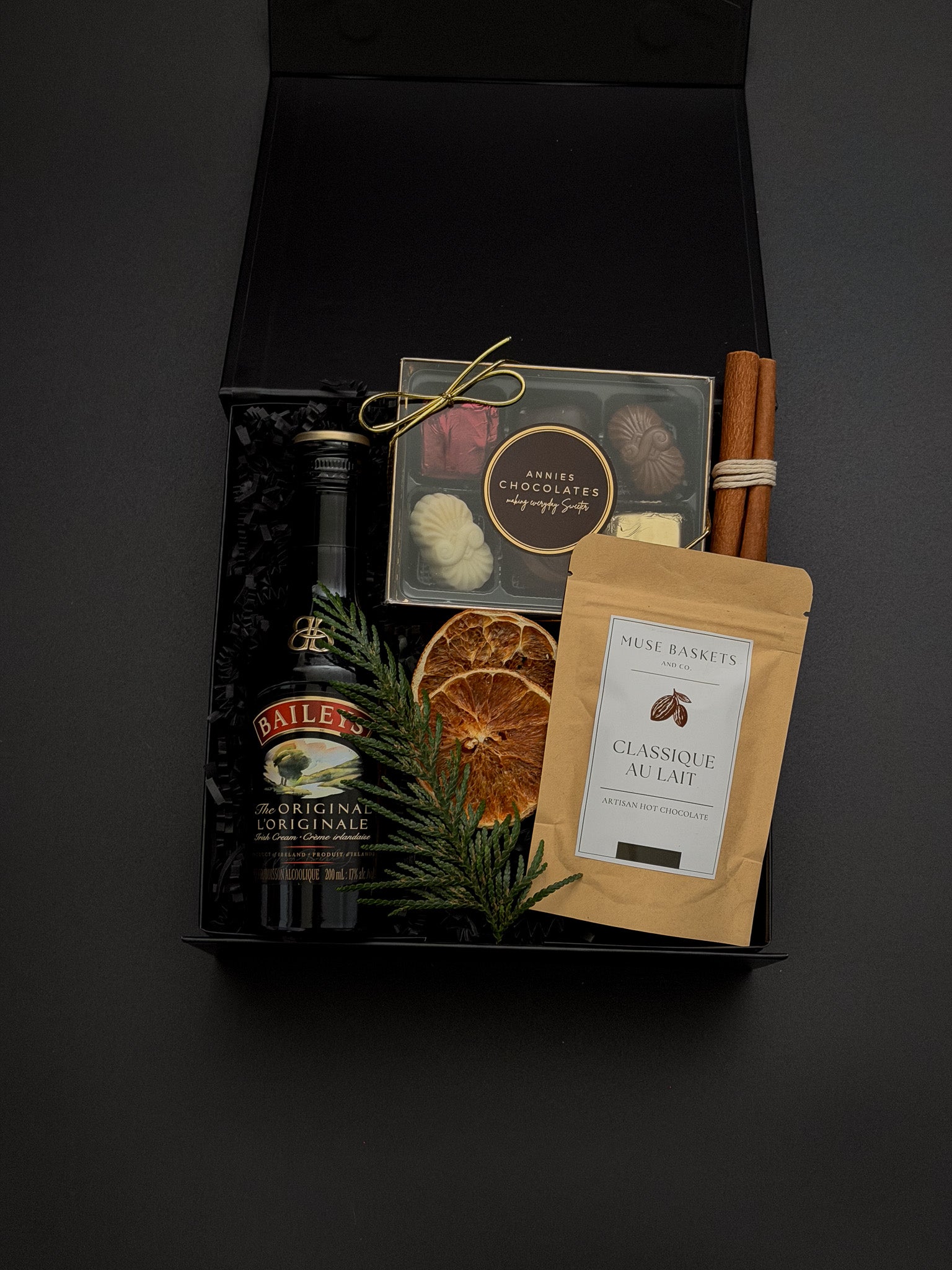 The Parlour Christmas gift box by Muse Baskets and Co. arranged with Baileys, gourmet chocolates, classic hot chocolate, cinnamon sticks and seasonal greenery.