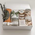 Élysée spa gift box by Muse Baskets and Co. shown close up at an angle, featuring Teakop Black Yunnan tea, a Muse candle by Aija, Sealuxe seaweed body scrub and face mask, Fresh Wife patchouli mint hand lotion, and lemon lavender bath tea with eucalyptus and an olive green ribbon, a refined thank you and employee appreciation gift from Canadian makers.