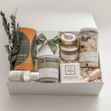 Élysée spa gift box by Muse Baskets and Co. shown close up at an angle, featuring Teakop Black Yunnan tea, a Muse candle by Aija, Sealuxe seaweed body scrub and face mask, Fresh Wife patchouli mint hand lotion, and lemon lavender bath tea with eucalyptus and an olive green ribbon, a refined thank you and employee appreciation gift from Canadian makers.