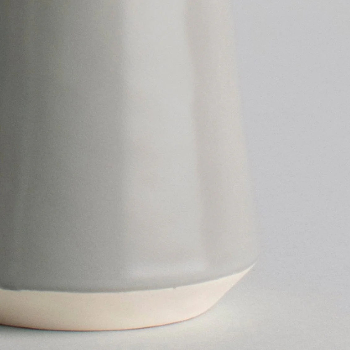Close-up of a gray ceramic cup with a beige base on a light gray background