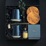 The Lennox gift box by Muse Baskets and Co. viewed close up at an angle, showing two midnight blue Fable mugs, two olive wood coasters, a VIS myrrh, amber, and sandalwood candle by Vancouver Candle Co., a gold candle snuffer, and black tipped matches in an apothecary jar with eucalyptus in a black box, a refined possession day, homeowner welcome, and development possession gift.