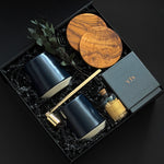 The Lennox gift box by Muse Baskets and Co. shown from above, featuring two midnight blue Fable mugs, two olive wood coasters, a VIS candle by Vancouver Candle Co., a gold candle snuffer, and black tipped matches in an apothecary jar with eucalyptus on black fill in a black box, a refined realtor closing gift, possession day gift, and homeowner welcome gift.