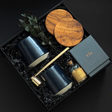 The Lennox gift box by Muse Baskets and Co. shown from above, featuring two midnight blue Fable mugs, two olive wood coasters, a VIS candle by Vancouver Candle Co., a gold candle snuffer, and black tipped matches in an apothecary jar with eucalyptus on black fill in a black box, a refined realtor closing gift, possession day gift, and homeowner welcome gift.