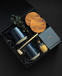 The Lennox gift box by Muse Baskets and Co. shown from above, featuring two midnight blue Fable mugs, two olive wood coasters, a VIS candle by Vancouver Candle Co., a gold candle snuffer, and black tipped matches in an apothecary jar with eucalyptus on black fill in a black box, a refined realtor closing gift, possession day gift, and homeowner welcome gift.