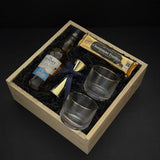The Belgravia executive gift basket by Muse Baskets and Co. featuring The Glenlivet Founder's Reserve Single Malt Scotch, two Viski Meridian gold-rimmed crystal lowball tumblers, a gold shot jigger with navy blue ribbon, and Roger's Chocolates Dark Chocolate Champagne Truffles, arranged in a signature locally sourced wood gift box with black crinkle fill, realtor closing gift and corporate gift, Vancouver, BC.
