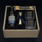 The Belgravia luxury corporate gift basket by Muse Baskets and Co. featuring The Glenlivet Founder's Reserve 1824 Single Malt Scotch Whisky, two Viski Meridian gold-rimmed crystal lowball tumblers, a gold shot jigger tied with a navy satin ribbon, and Roger's Chocolates Dark Chocolate Champagne Truffles, styled in a natural wood gift box with black crinkle fill, possession day gift and executive gift, Vancouver, BC.