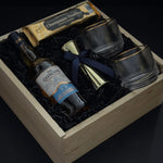 The Belgravia bespoke whisky gift set by Muse Baskets and Co. featuring The Glenlivet Founder's Reserve Single Malt Scotch, Viski Meridian gold-rimmed crystal tumblers, a gold double-sided shot jigger with navy blue bow, and Roger's Chocolates Dark Chocolate Champagne Truffles, presented in a signature locally sourced wood gift box, realtor closing gift and branded corporate gift, Vancouver, BC.