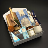 Fireside Provisions holiday gift box by Muse Baskets and Co., with tea, honey, artisan chocolate and stoneware in a Signature Pearl White gift box.