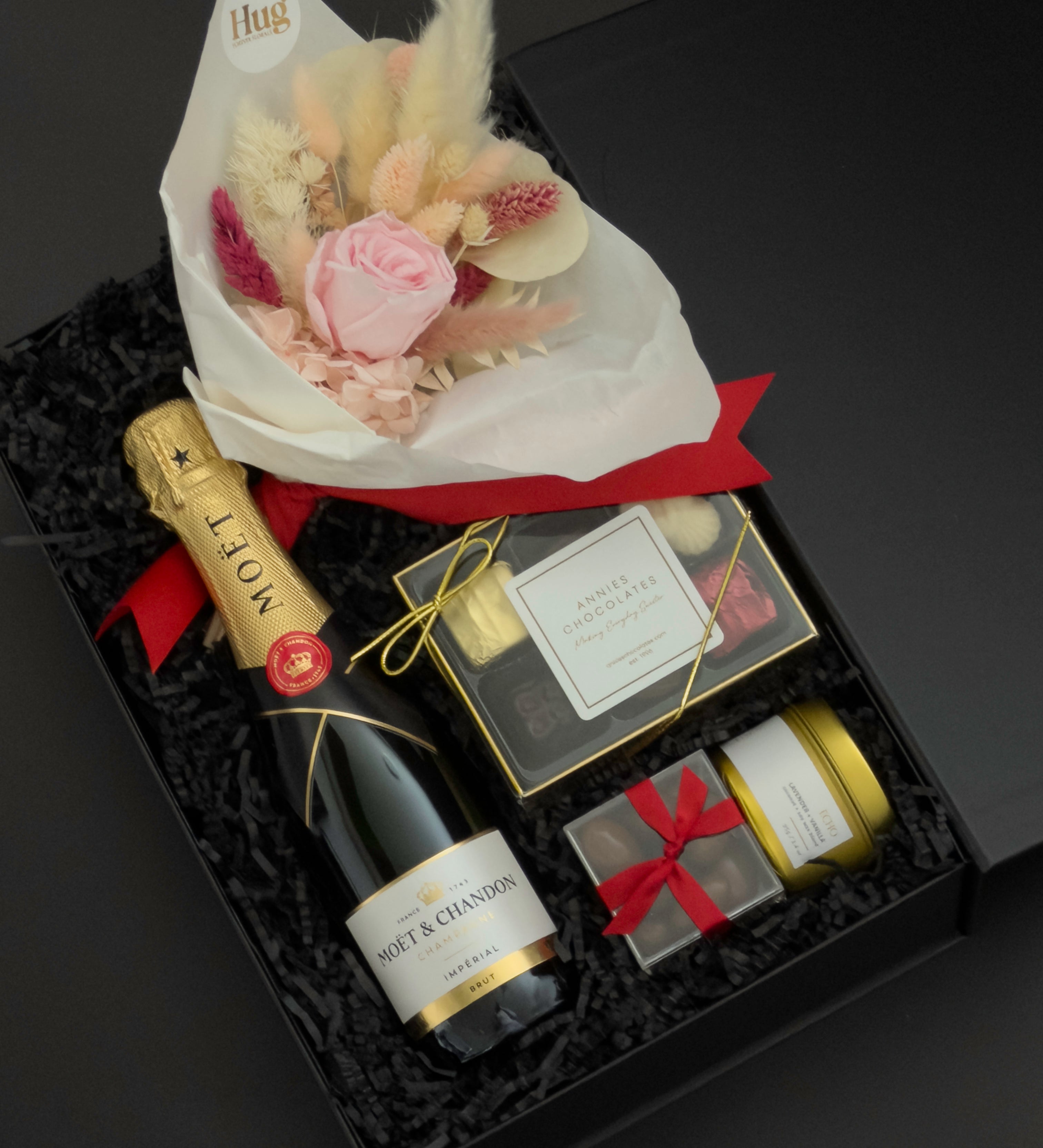 Elegant black gift box with Moët & Chandon champagne, preserved floral bouquet, chocolates, and candle arranged for a romantic celebration