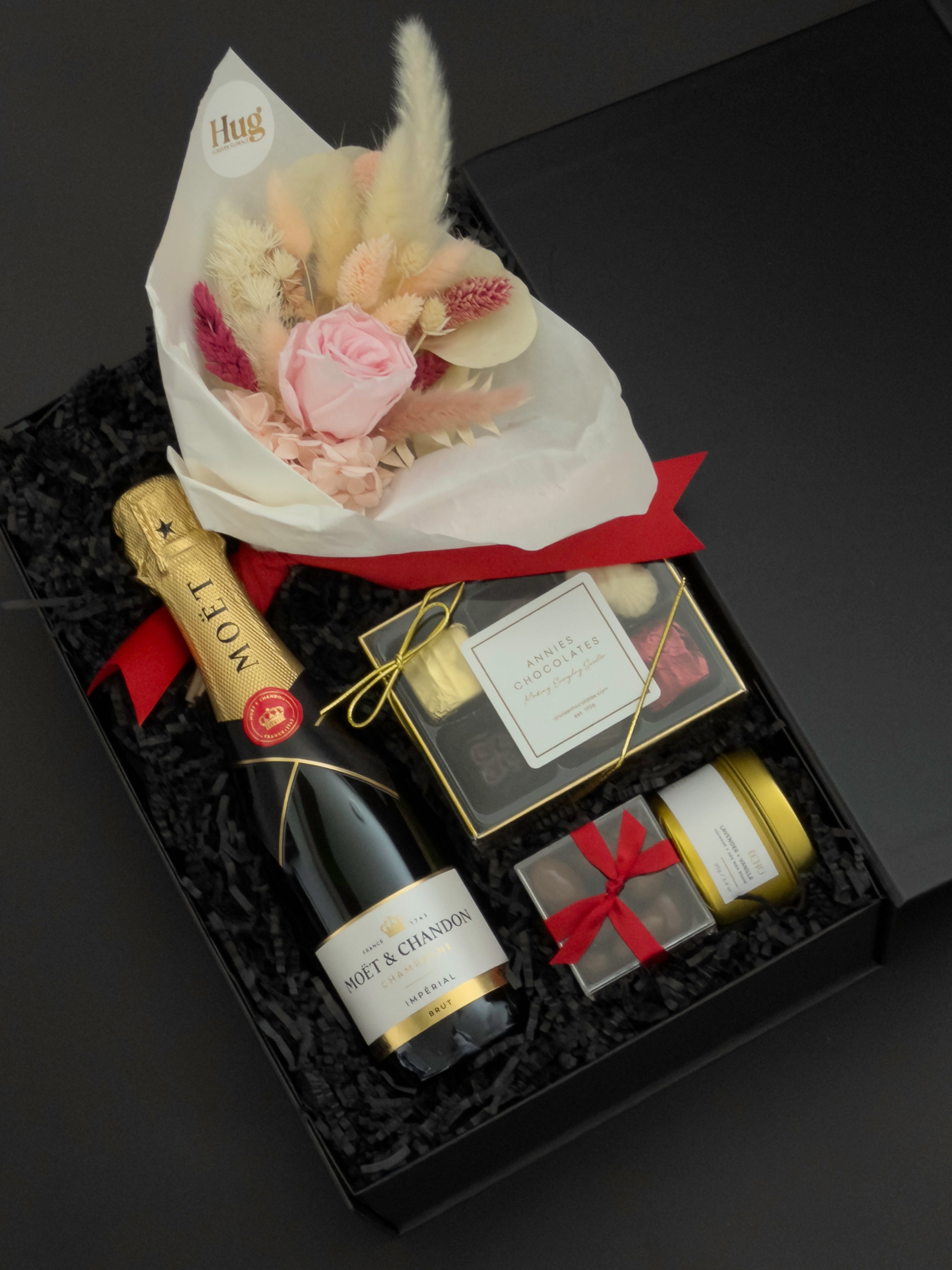 Elegant black gift box with Moët & Chandon champagne, preserved floral bouquet, chocolates, and candle arranged for a romantic celebration