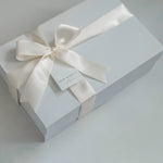 White gift box with a satin ribbon and tag on a light gray background
