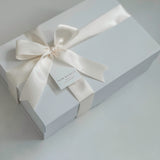 White gift box with a satin ribbon and tag on a light gray background