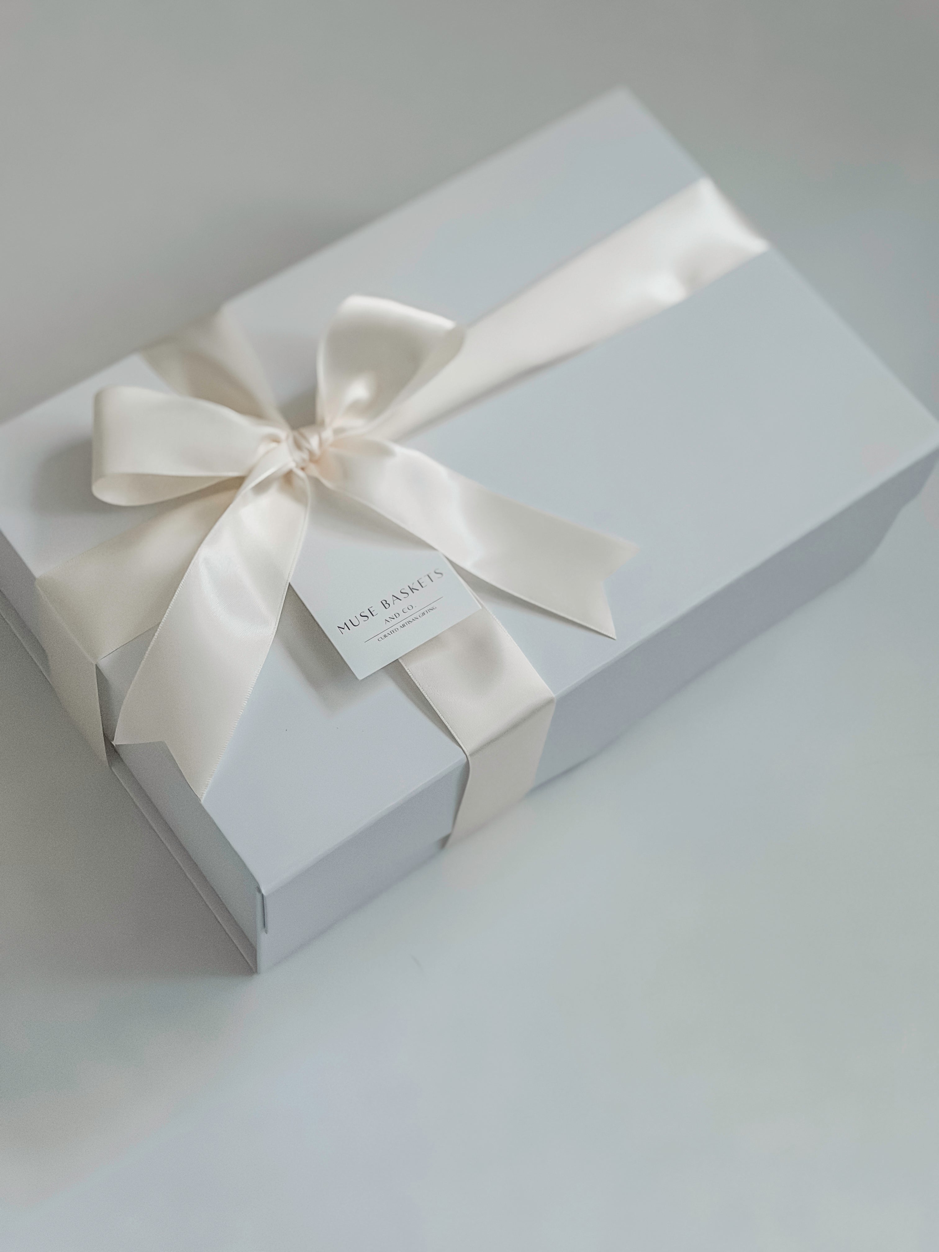White gift box with a satin ribbon and tag on a light gray background
