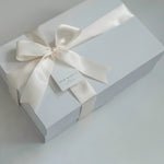White gift box with a satin ribbon and tag on a light gray background