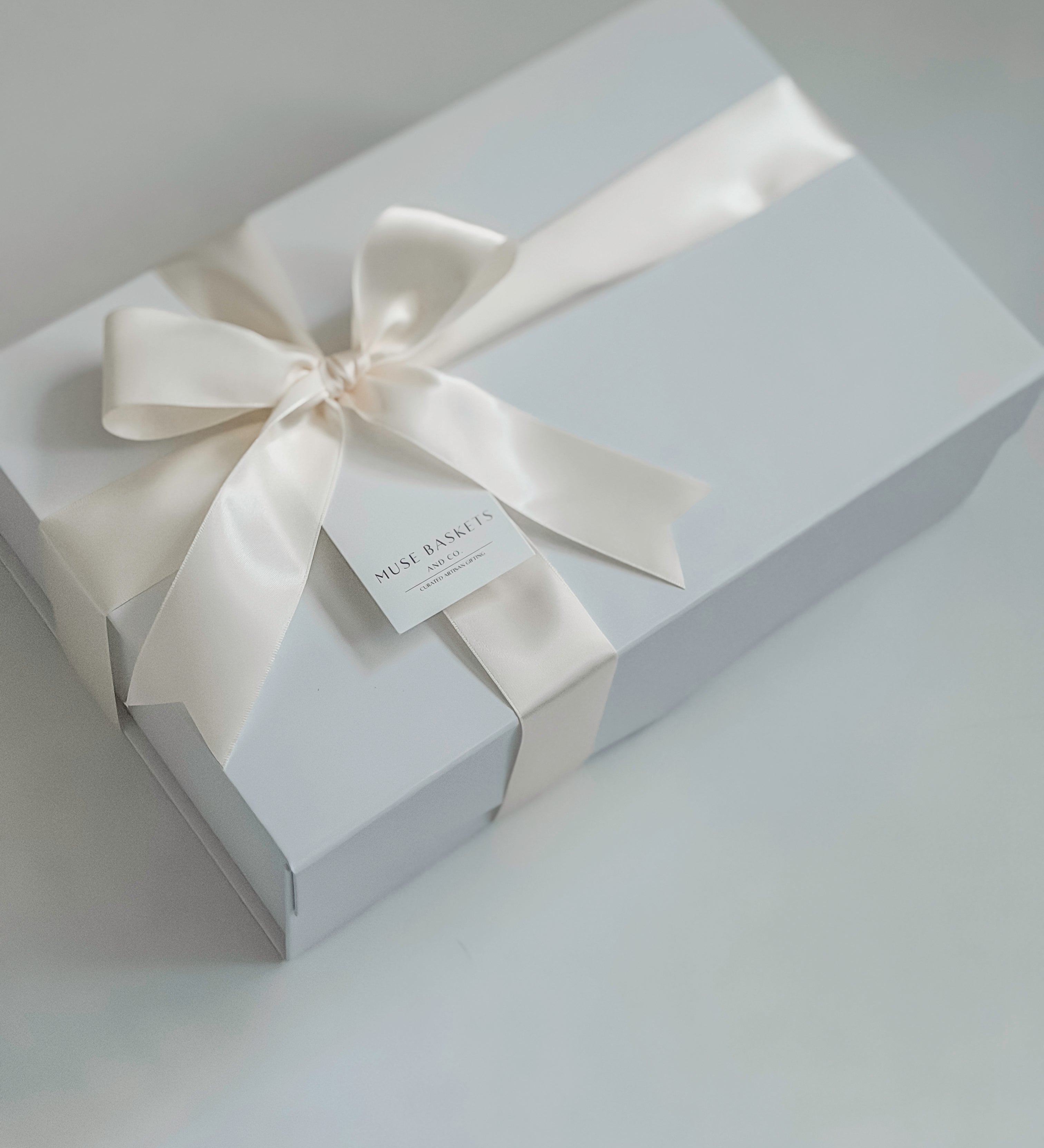 White gift box with a satin ribbon and tag on a light gray background