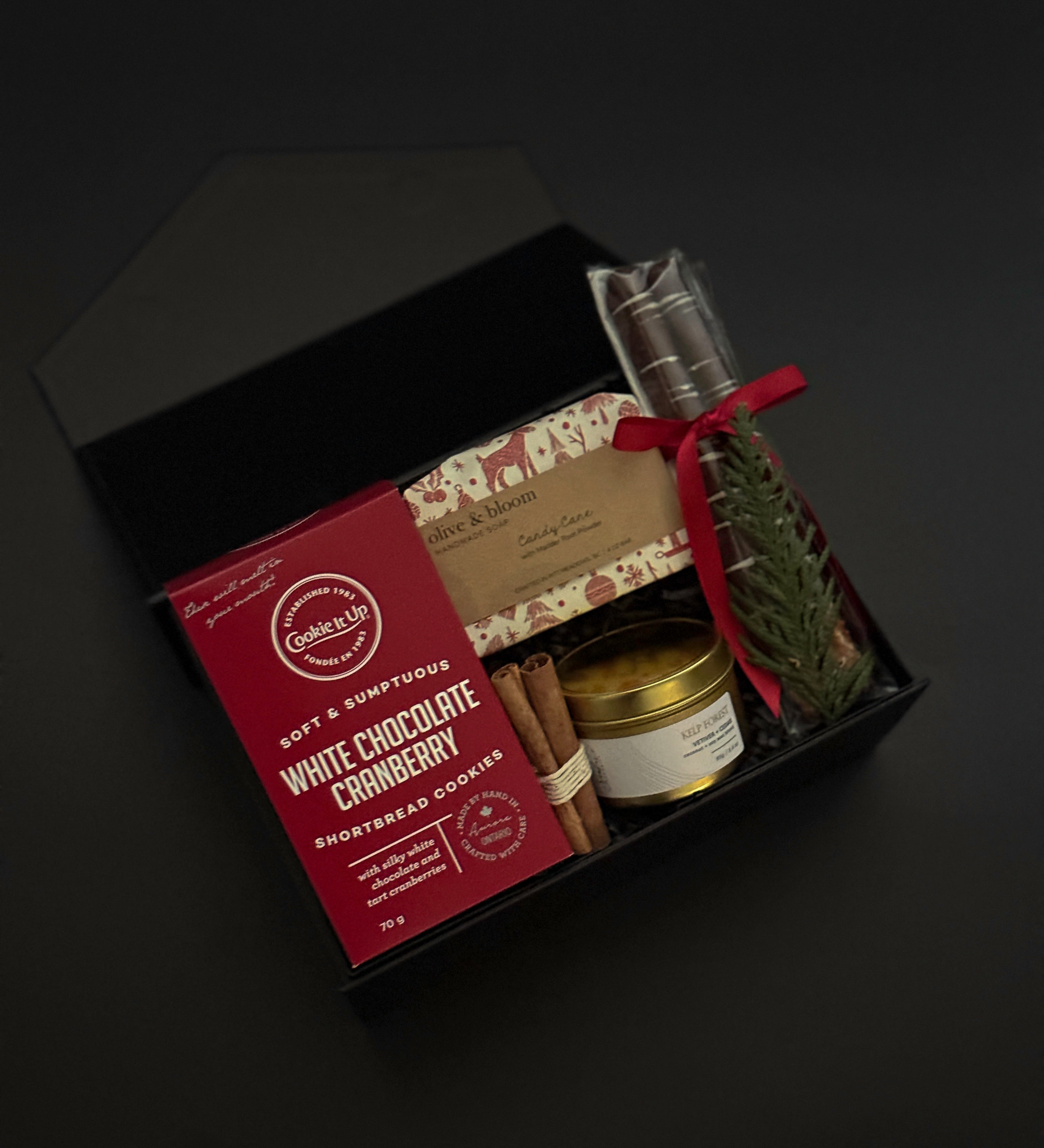 Gift set with white chocolate cranberry cookies, a candle, and other items in a black box on a dark background.