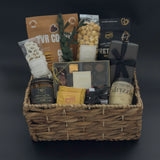 Luxury metropolitan gift basket featuring gourmet chocolates, cookies, raw honey, and forest fir candle arranged in a woven basket with black satin ribbon