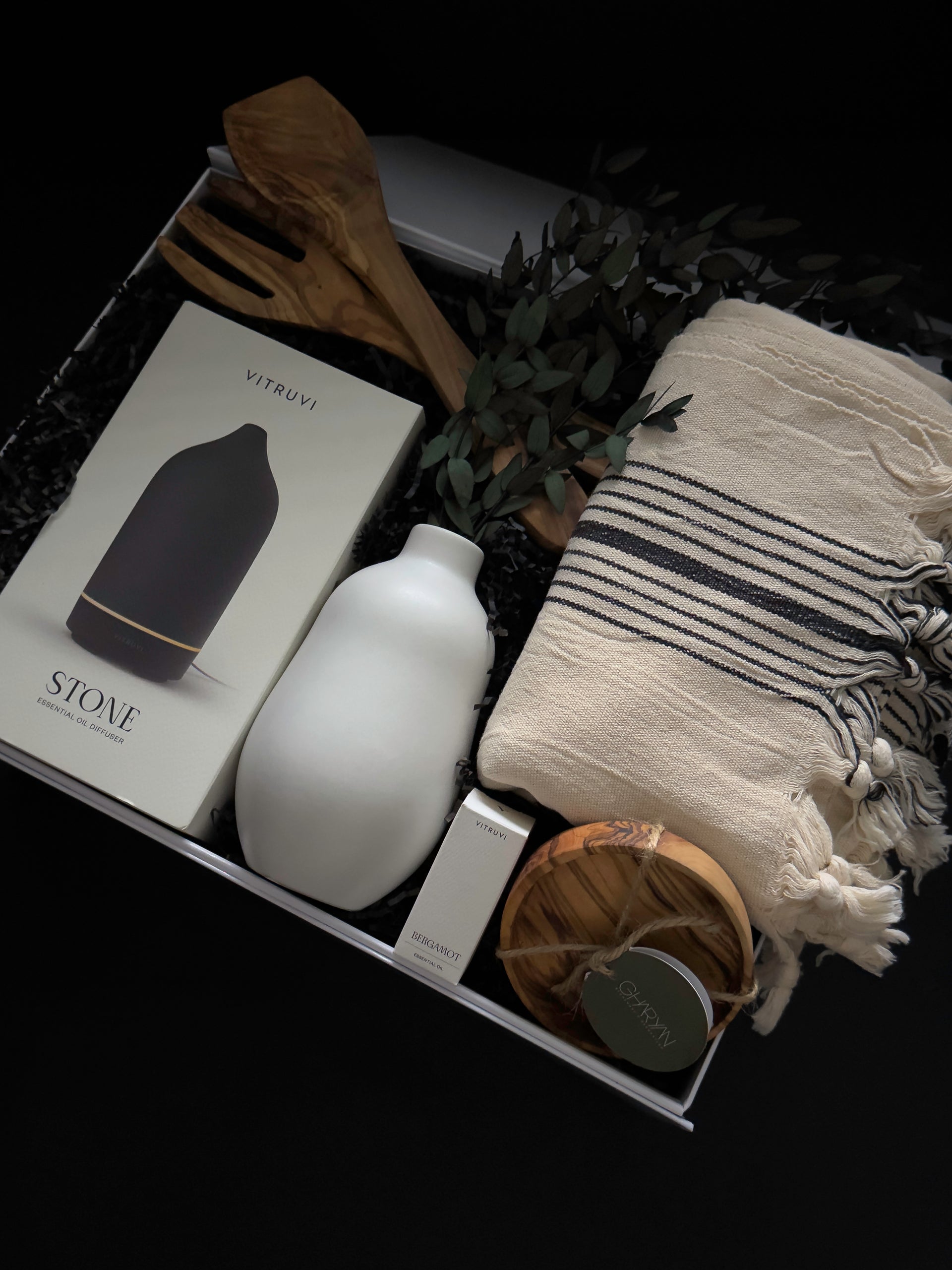 Close up of luxury housewarming gift box with Vitruvi diffuser Turkish towel and olive wood snack bowl by Muse Baskets and Co