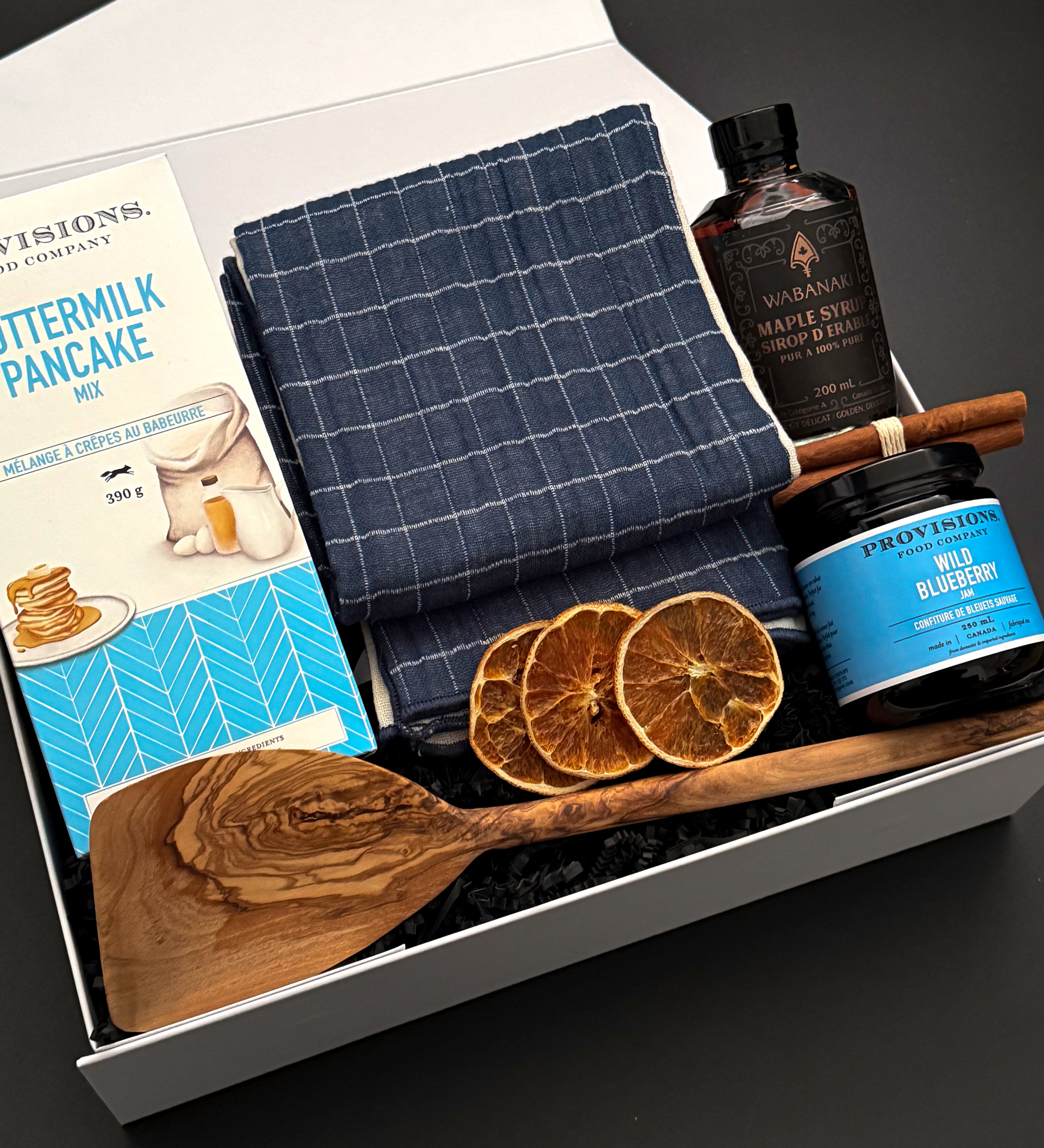 Muse Baskets and Co. holiday breakfast gift box with an olive wood spatula, navy checkered towel and Canadian pantry favourites.