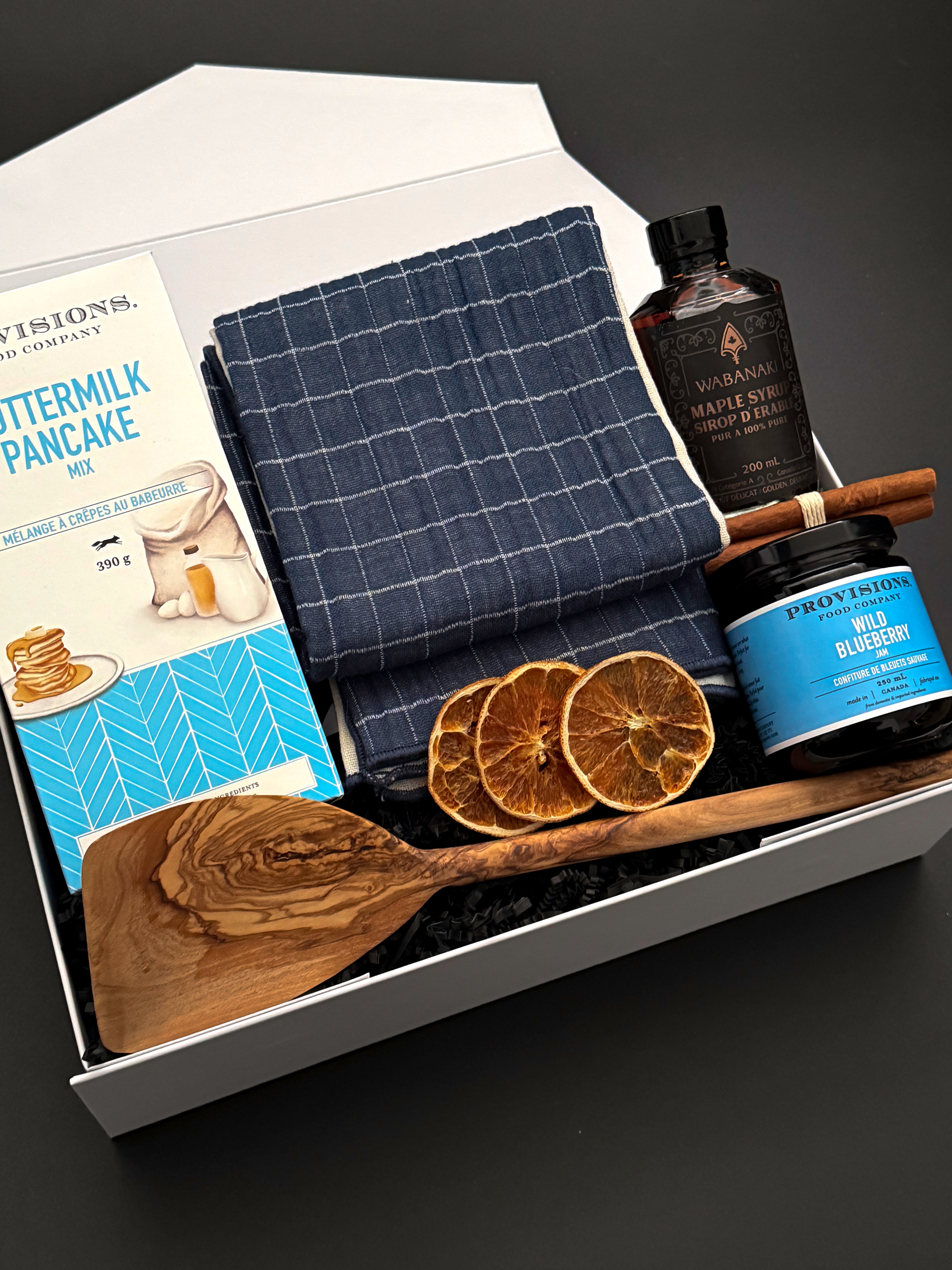 Muse Baskets and Co. holiday breakfast gift box with an olive wood spatula, navy checkered towel and Canadian pantry favourites.