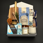 Fireside Provisions by Muse Baskets and Co., a Canadian holiday gift box with Camembert, cashews and chocolate pretzels arranged with seasonal greenery.