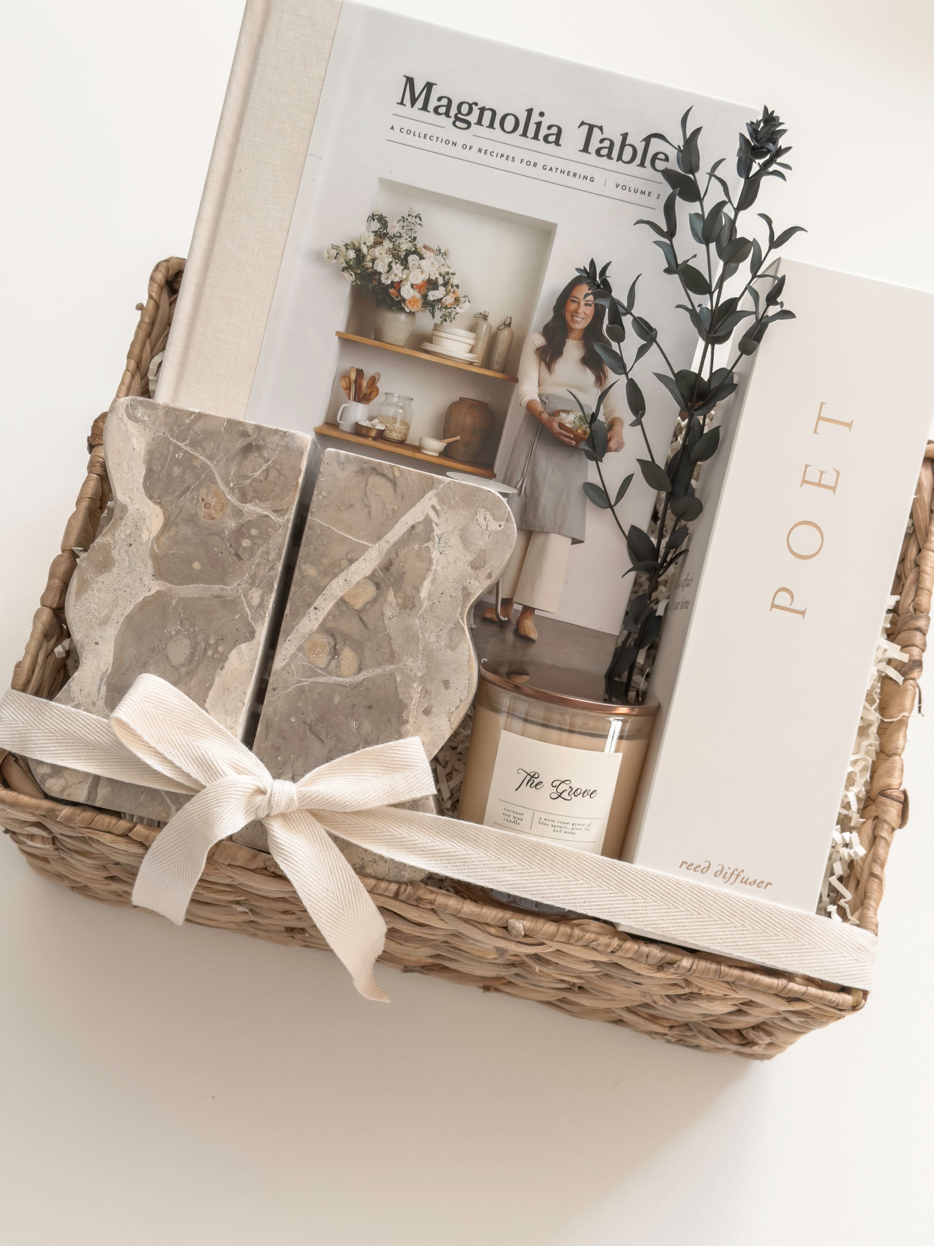 The Estate client appreciation gift with architectural bookends, Magnolia Table and Poet Farm Co. home fragrance arranged in a wicker basket.