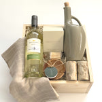 The Harvest Host Thanksgiving gift basket by Muse Baskets and Co. featuring Mission Hill Sauvignon Blanc, a Vancouver Candle Co. candle, matches, stoneware olive oil dispenser, marble salt and pepper shakers, olive wood ramekin and grey dishtowels in a wood gift box.