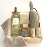 The Harvest Host Thanksgiving gift basket by Muse Baskets and Co. featuring Mission Hill Sauvignon Blanc, a Vancouver Candle Co. candle, matches, stoneware olive oil dispenser, marble salt and pepper shakers, olive wood ramekin and grey dishtowels in a wood gift box.