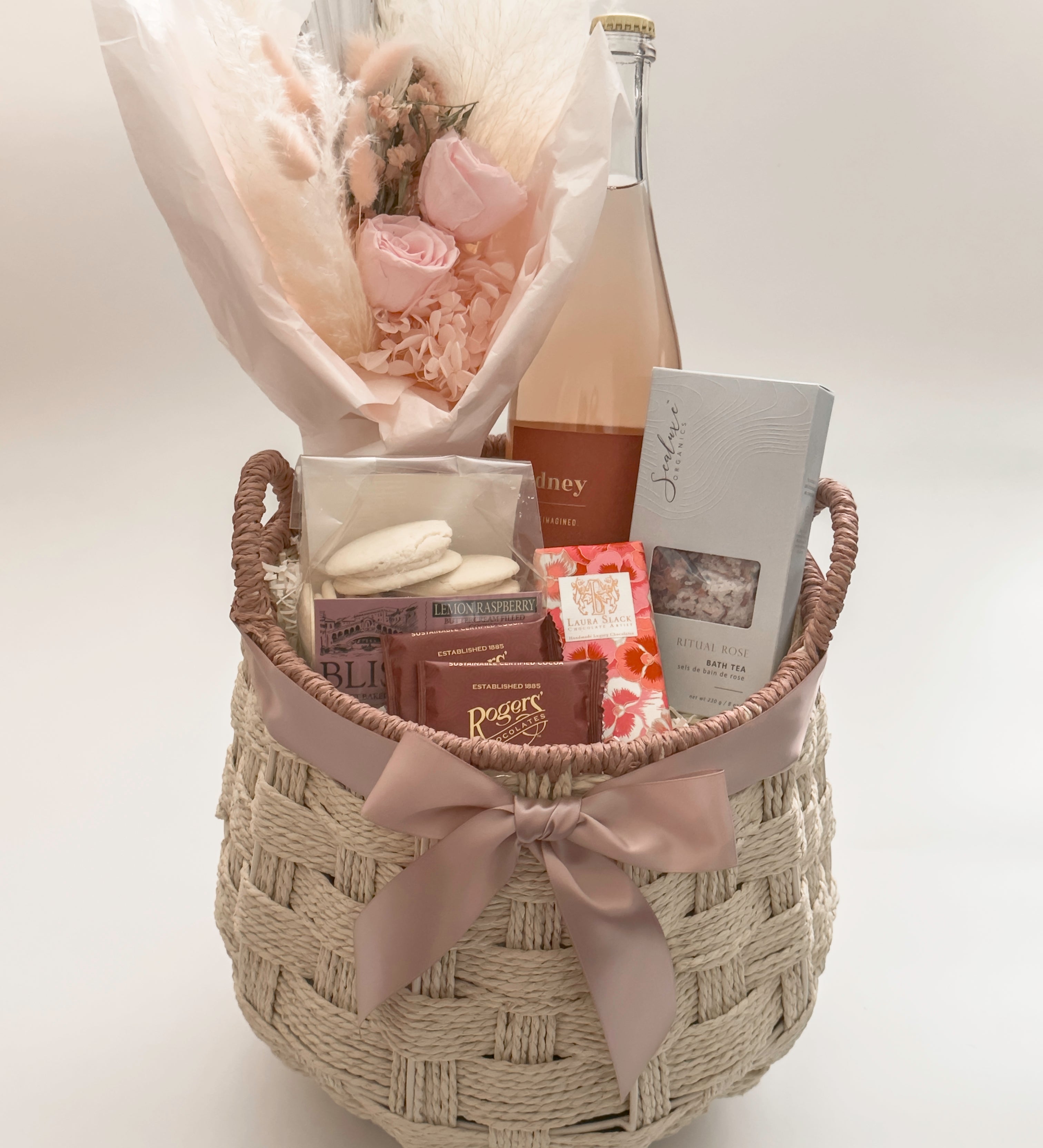 In Her Bloom luxury Mother's Day and client appreciation gift basket for her featuring Sidney Sparkling Rosé, preserved blush rose bouquet by Hugme Florals, Sealuxe Organics Ritual Rose Bath Tea, and Canadian artisan chocolates in a handwoven wicker basket with mauve satin ribbon by Muse Baskets and Co Vancouver