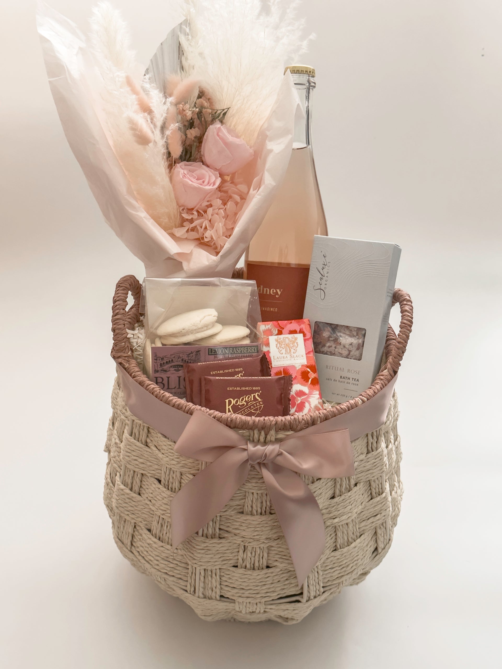 In Her Bloom luxury Mother's Day and client appreciation gift basket for her featuring Sidney Sparkling Rosé, preserved blush rose bouquet by Hugme Florals, Sealuxe Organics Ritual Rose Bath Tea, and Canadian artisan chocolates in a handwoven wicker basket with mauve satin ribbon by Muse Baskets and Co Vancouver