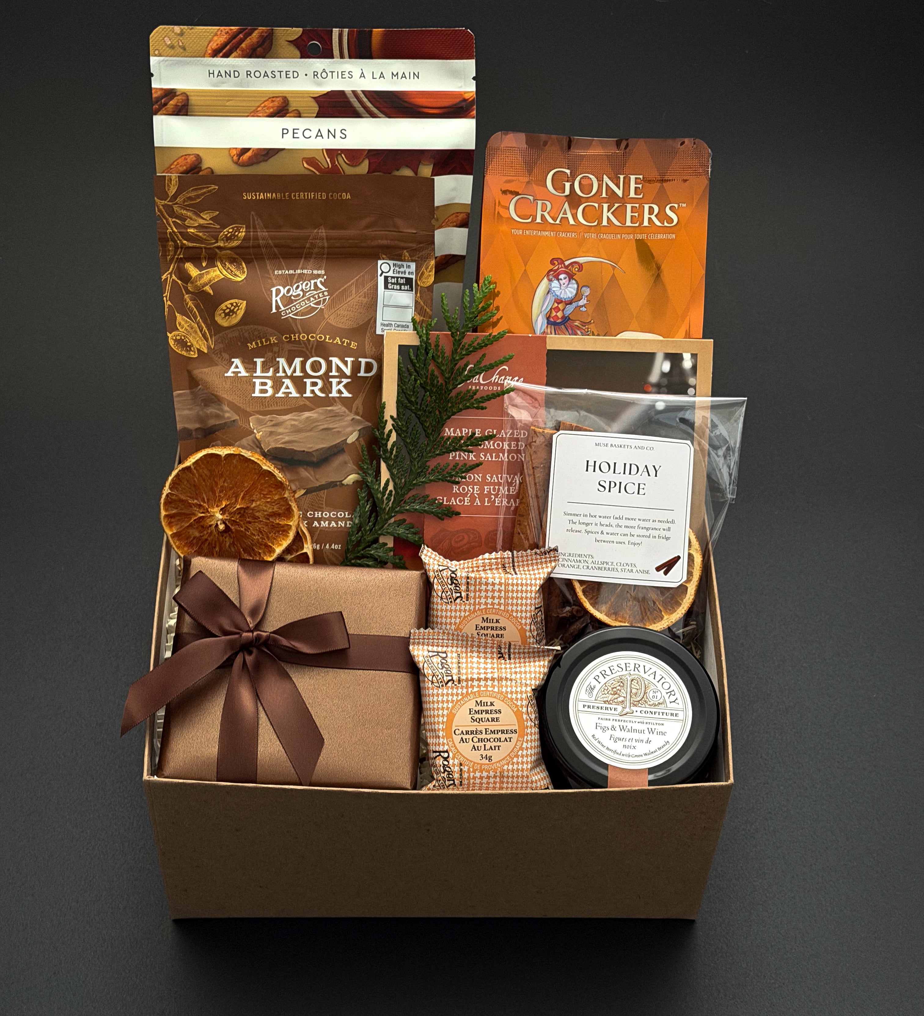 Cedar & Clove holiday gift box by Muse Baskets and Co. with maple pecans, brie, salmon and chocolate in a kraft box finished with brown satin ribbon.