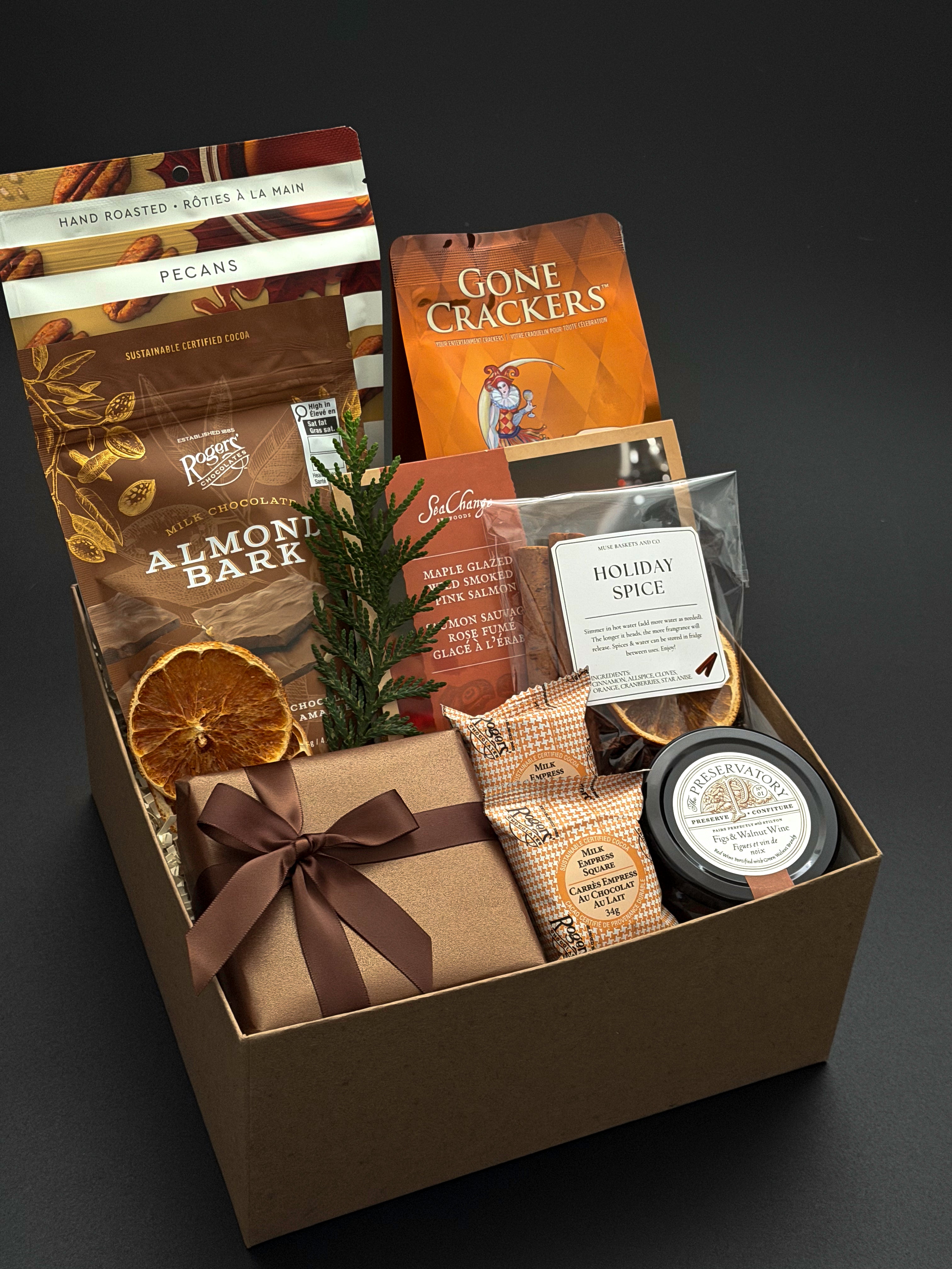 Cedar & Clove holiday gift box by Muse Baskets and Co. with Fig & Walnut Wine Preserve, savoury crackers and brie wrapped in brown paper and ribbon.