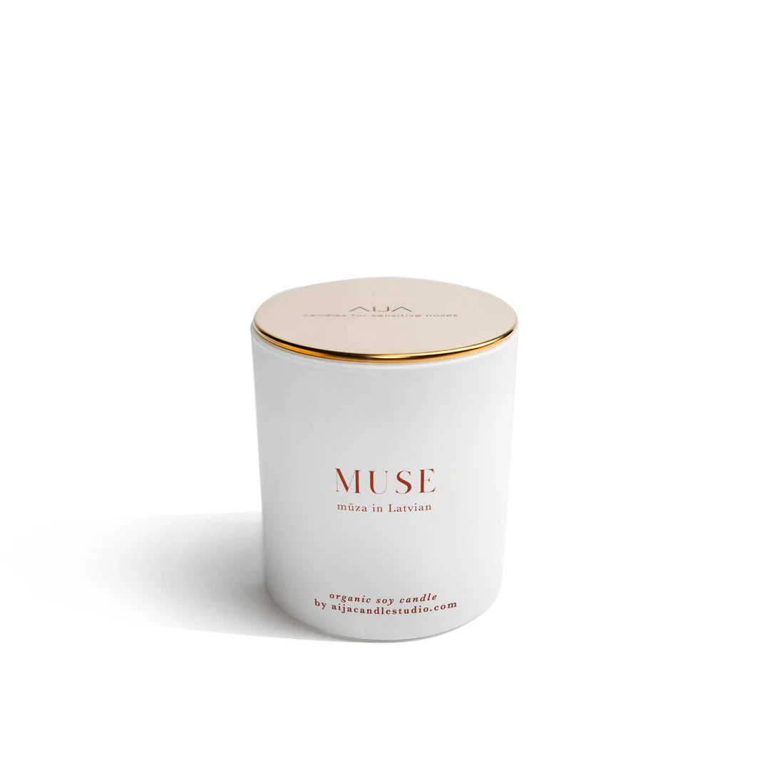 White candle with gold lid labeled 'MUSE' on a white background