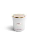 White candle with gold lid labeled 'MUSE' on a white background