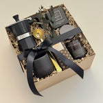 Oro Nero luxury coffee gift box by Muse Baskets and Co. shown at an angle, featuring a Grosche Moka pot, gold coffee scoop, handmade black stoneware cup, So charcoal cleansing bar, Laura Slack chocolate, and a James Street Co. teakwood and tobacco candle, arranged in a kraft box with eucalyptus and a black satin bow. A Canadian artisan client gift and corporate gift.