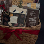 Gift basket with assorted items including a box of chocolates and a bag of cookies on a dark background.