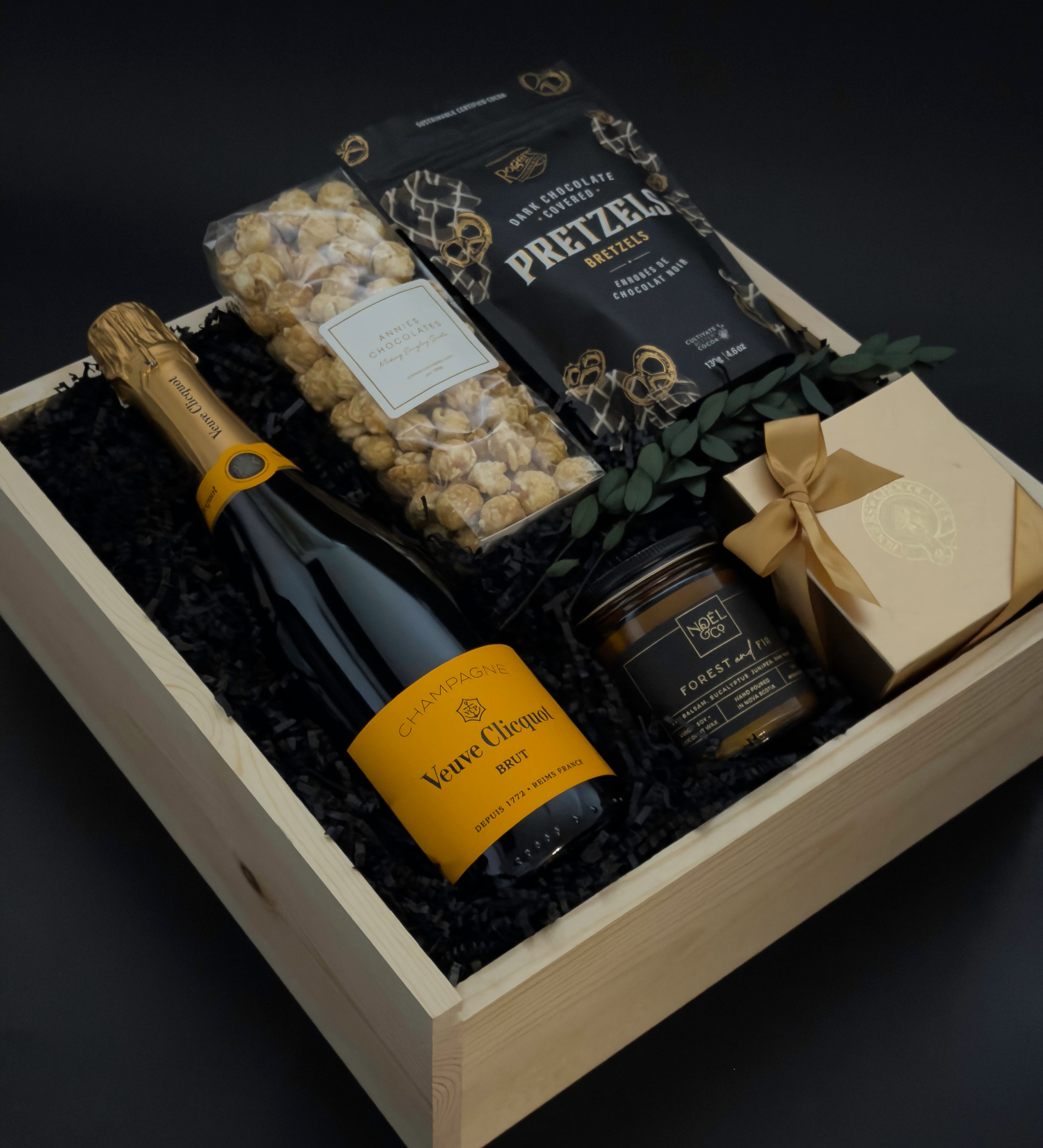 Gift basket with champagne, pretzels, and other snacks on a dark background
