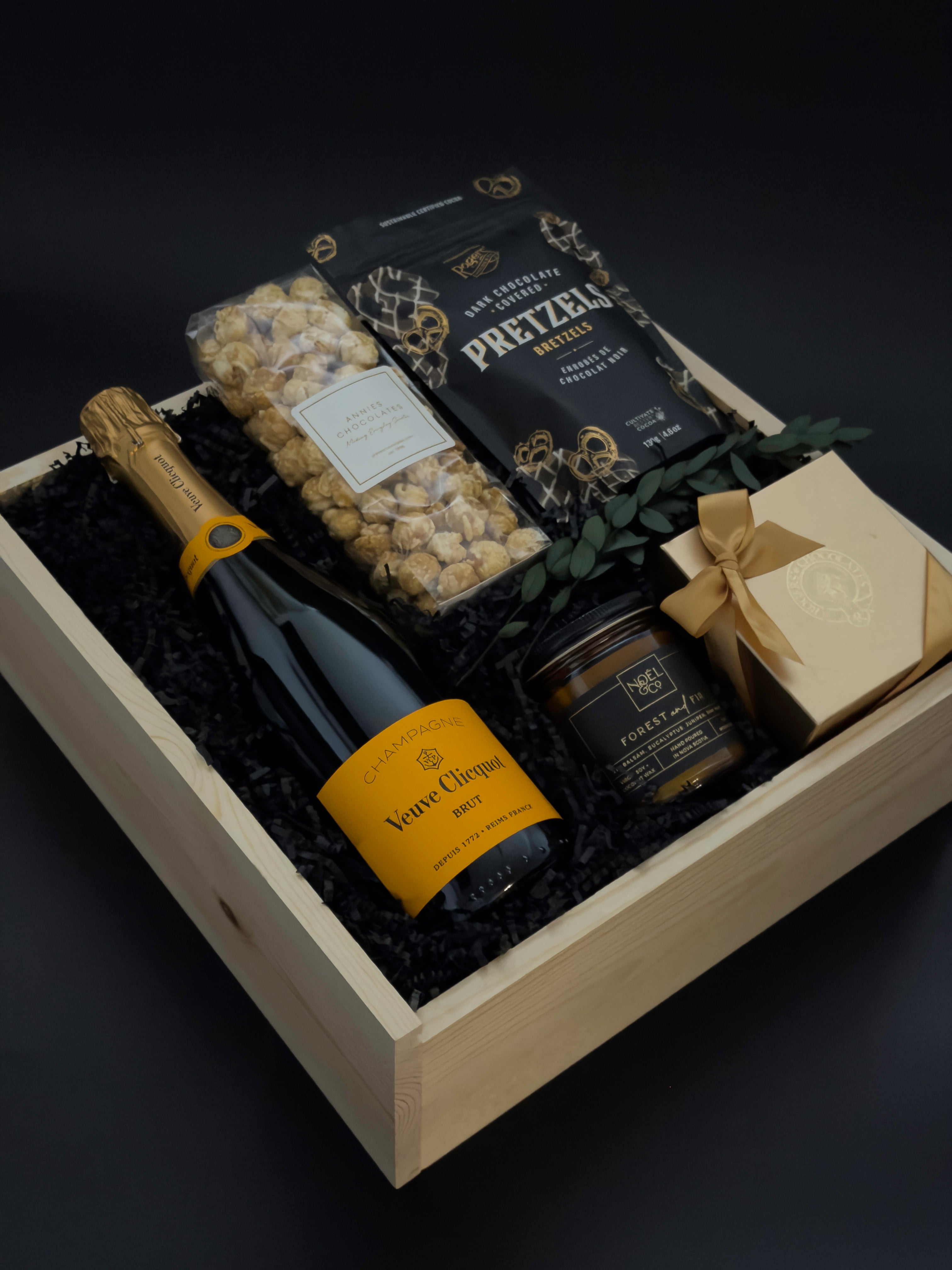 Gift basket with champagne, pretzels, and other snacks on a dark background