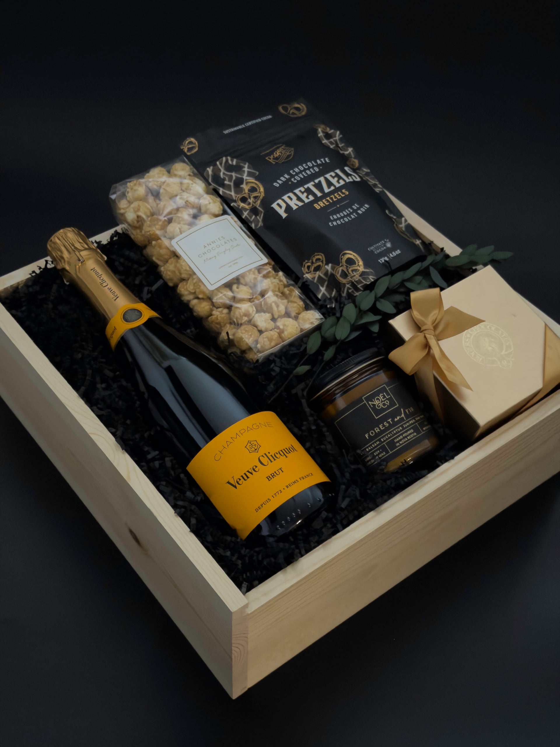 Gift basket with champagne, pretzels, and other snacks on a dark background