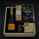 Gift basket with champagne, pretzels, popcorn, and a card on a dark background