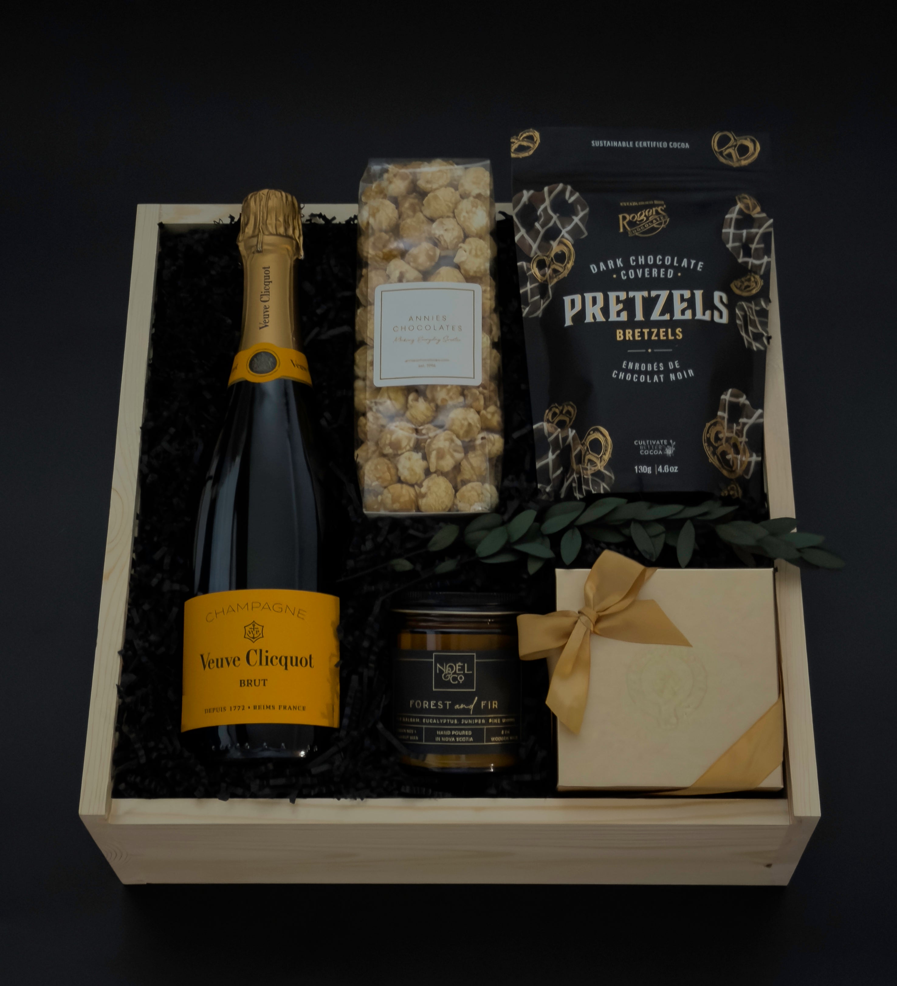 Gift basket with champagne, pretzels, popcorn, and a card on a dark background
