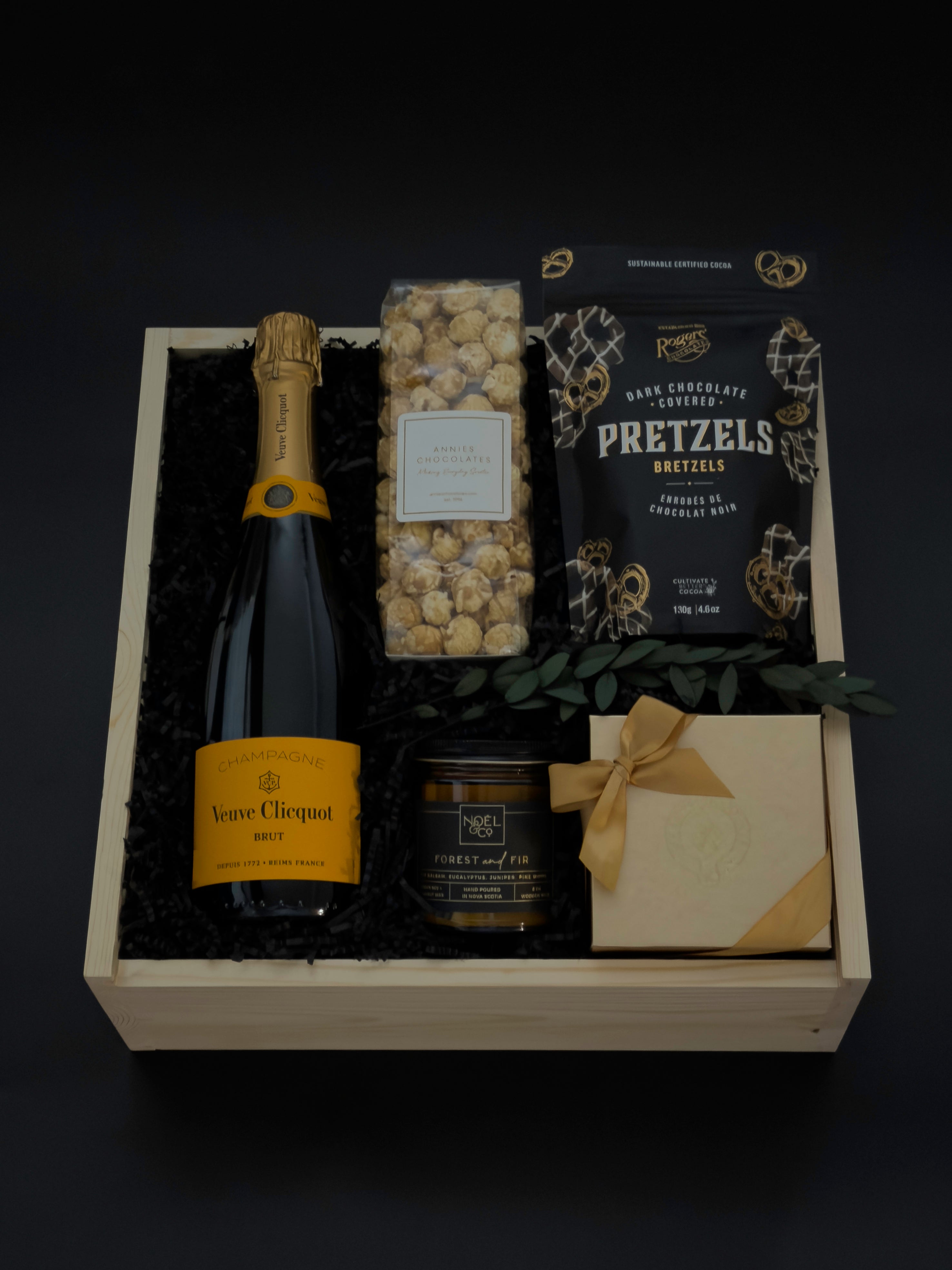 Gift basket with champagne, pretzels, popcorn, and a card on a dark background