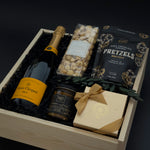 Gift basket with champagne, snacks, and a bar of chocolate on a dark background