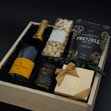Gift basket with champagne, snacks, and a bar of chocolate on a dark background