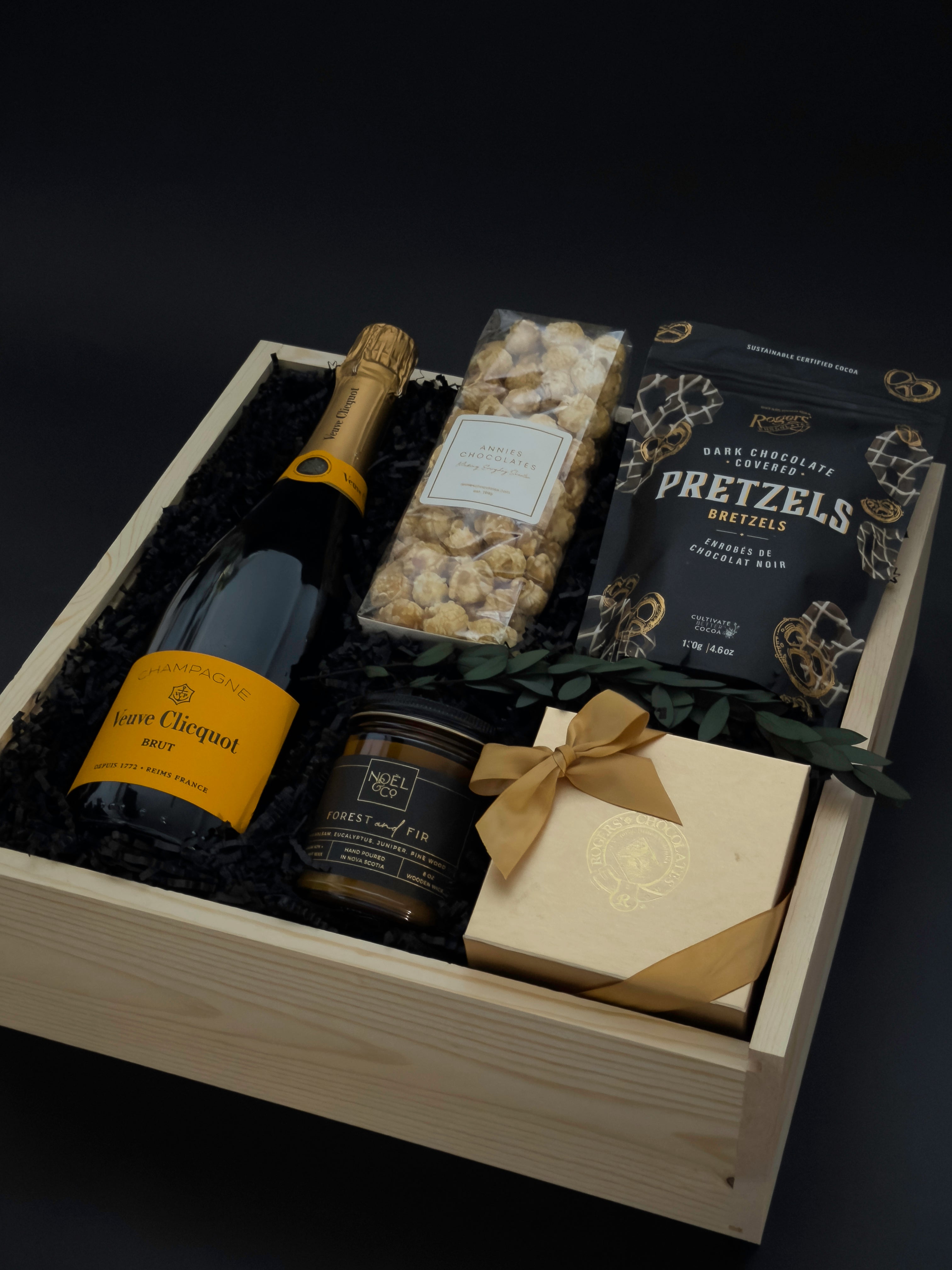 Gift basket with champagne, snacks, and a bar of chocolate on a dark background