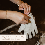 Person holding a white glove with text about organic cotton on a natural background